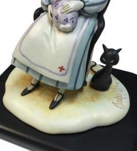 Nurse Figurine titled Loving Care is a P Buckley Moss figurine featuring a nurse holding a baby and giving comfort. Colors of lavender, blue, cream, golden for hair and black base and tiny cat. 