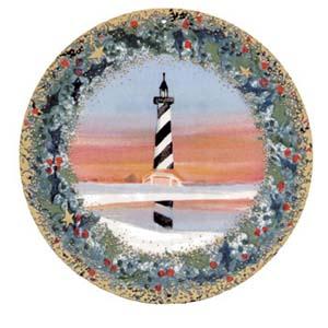 Cape Hatteras limited edition porcelain ornament by P Buckley Moss features the hatteras lighthouse against a peach and coral background within a wreath of greens, reds and golds.