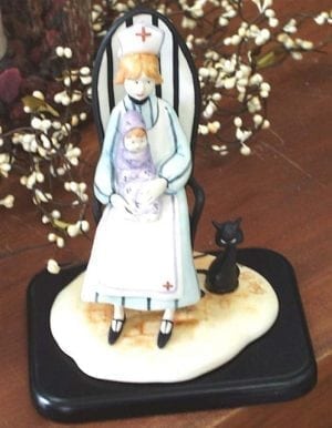 Nurse Figurine titled Loving Care is a P Buckley Moss figurine featuring a nurse holding a baby and giving comfort. Colors of lavender, blue, cream, golden for hair and black base and tiny cat.