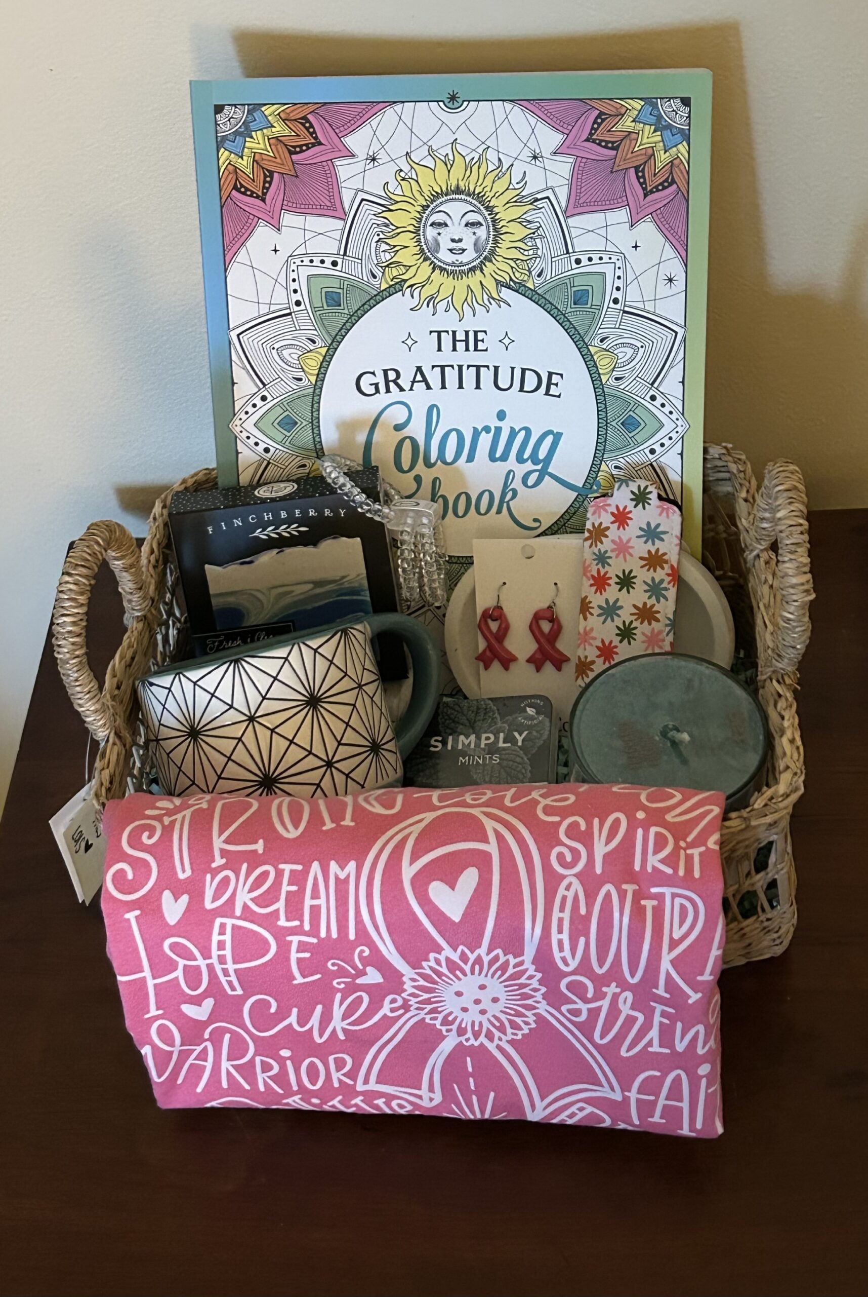 #4 RENEW Boutique Basket Kettering Health fundraiser basket with pink inspirational shirt, pink ribbon earrings, gratitude coloring book, candle, mug and self-care gifts.