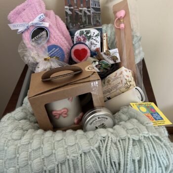#5 The Peddler House Waynesville Ohio with green throw, pink ribbon mug, Snoozies slippers, tea, preserves, candle and self-care gifts.